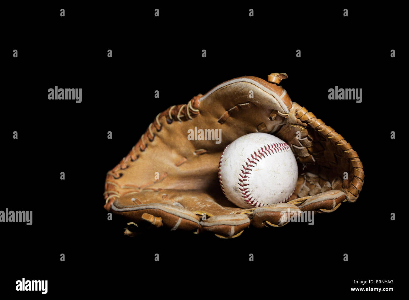 Ein abgenutzter Baseball sitzt im Inneren eines alten Baseballhandschuh auf einem einfarbigen schwarzen Hintergrund.  Bild wurde mit einer Lightpainting-Technik beleuchtet Stockfoto