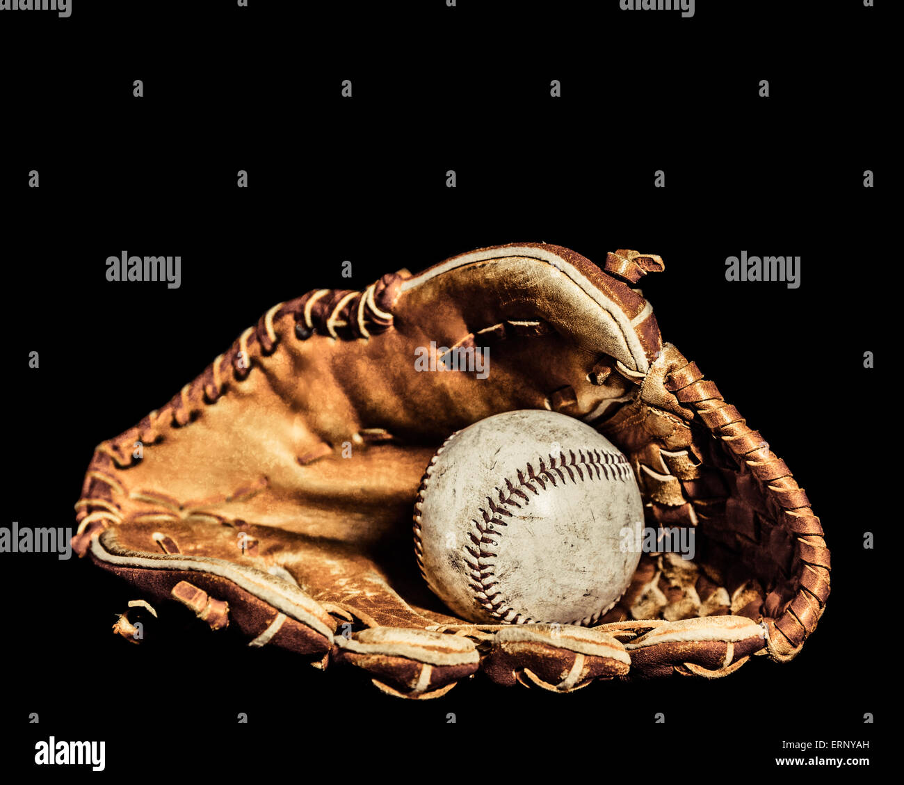 Ein abgenutzter Baseball sitzt im Inneren eines alten Baseballhandschuh auf einem einfarbigen schwarzen Hintergrund.  Bild wurde mit einer Lightpainting-Technik beleuchtet Stockfoto