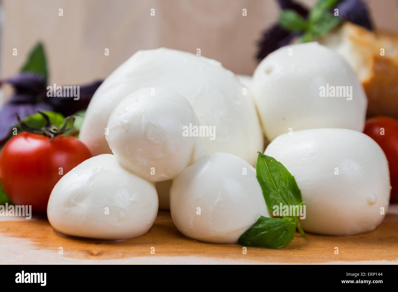 Kugeln Mozzarella unterschiedlicher Größe mit Cherry Tomaten, Brot und Basilikum auf hölzernen Hintergrund Stockfoto