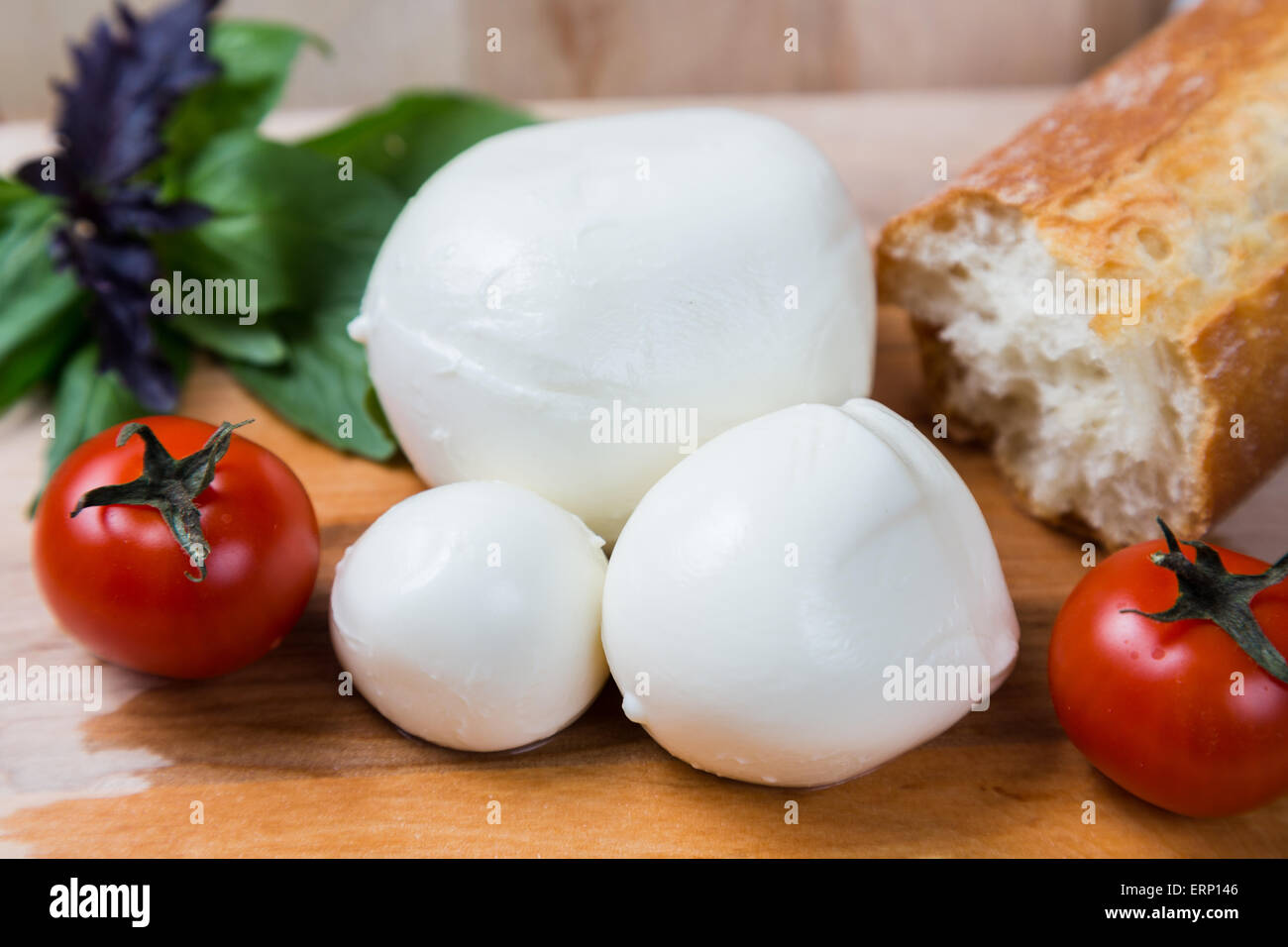 Kugeln Mozzarella unterschiedlicher Größe mit Cherry Tomaten, Brot und Basilikum auf hölzernen Hintergrund Stockfoto