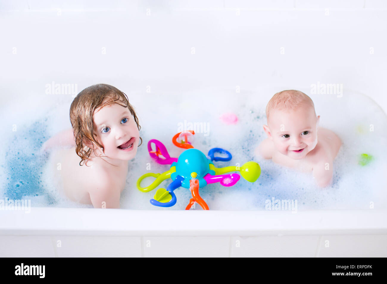 Lustige kleine Mädchen und ihr süßes Baby Bruder Spaß unter Bad spielen im Wasser mit Schaum mit bunten Spielzeug nach Dusche Stockfoto