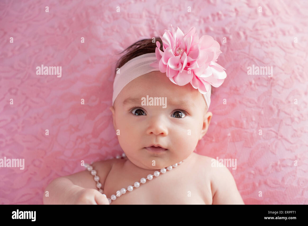Ein Porträt von einer Warnung, 3 Monate alten Baby Mädchen trägt einen großen, rosa, Blumen Haarband und Perlen. Sie liegt auf dem Rücken auf pin Stockfoto