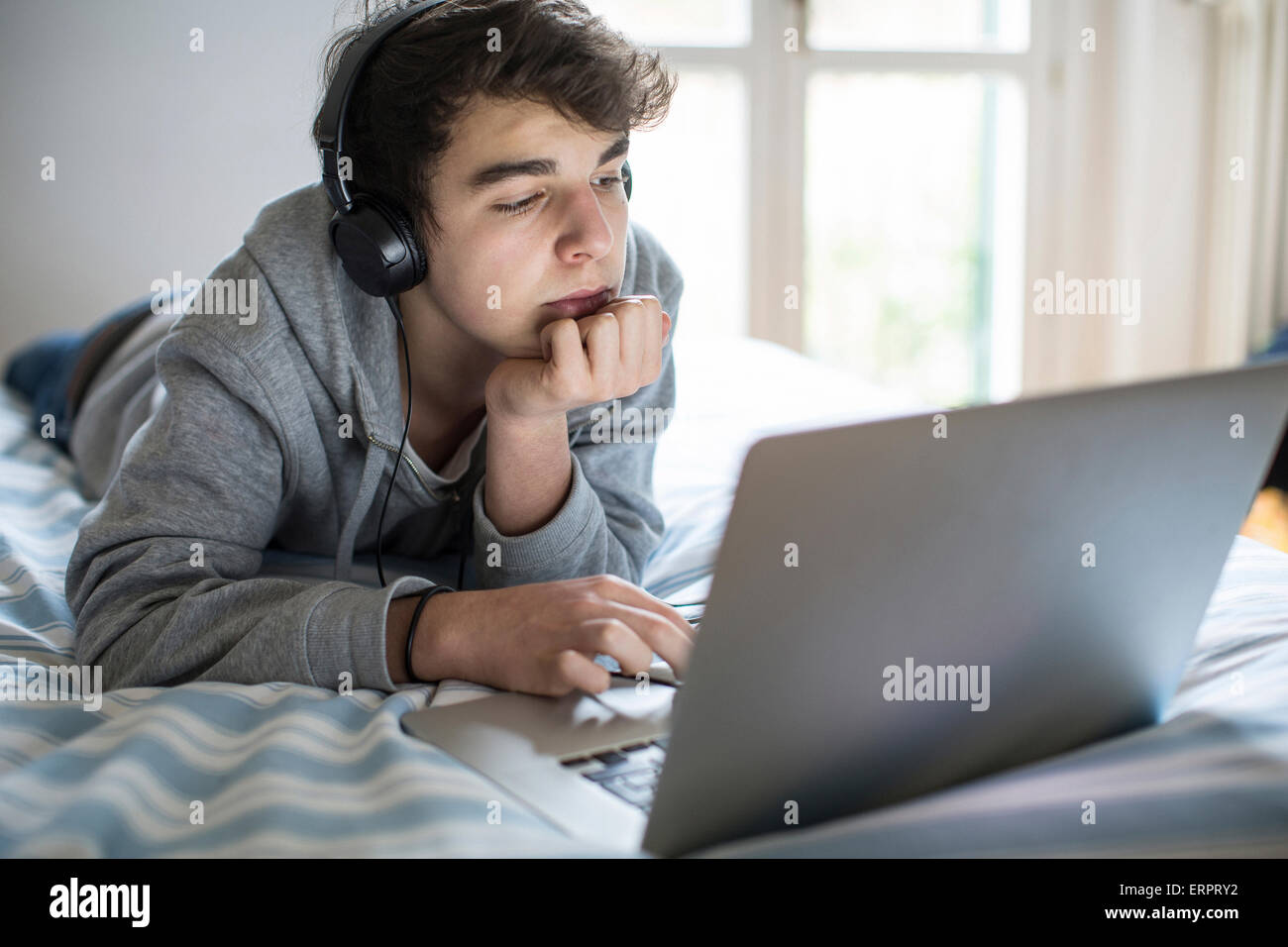 -MODELL VERÖFFENTLICHT. Junger Mann mit Laptop im Schlafzimmer. Stockfoto