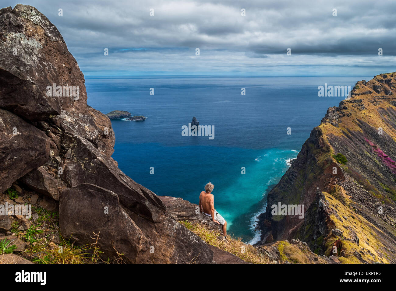 Rückseite ein Mann sitzt auf einer Klippe über dem Meer am Rand des Kraters Rano Kao, Osterinsel, Chile Stockfoto