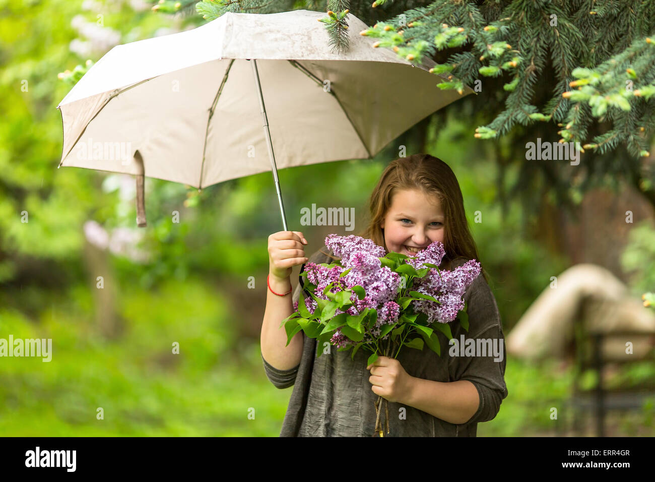 Teenager-Mädchen stehen unter einem Sonnenschirm mit einem Bouquet von Flieder in der Hand. Stockfoto