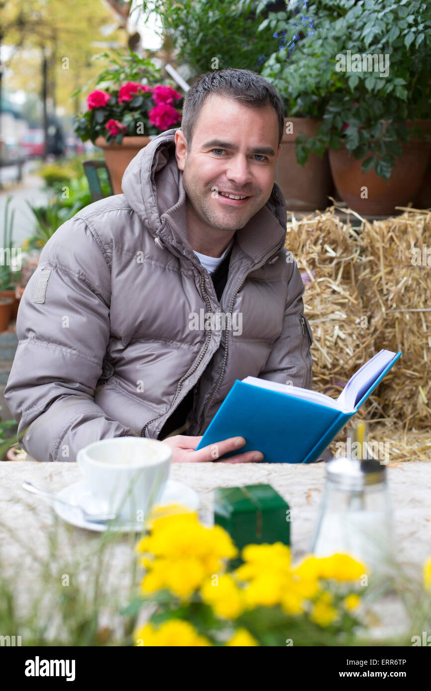 gut aussehender Mann draußen in einem Café sitzen und ein Buch zu lesen Stockfoto