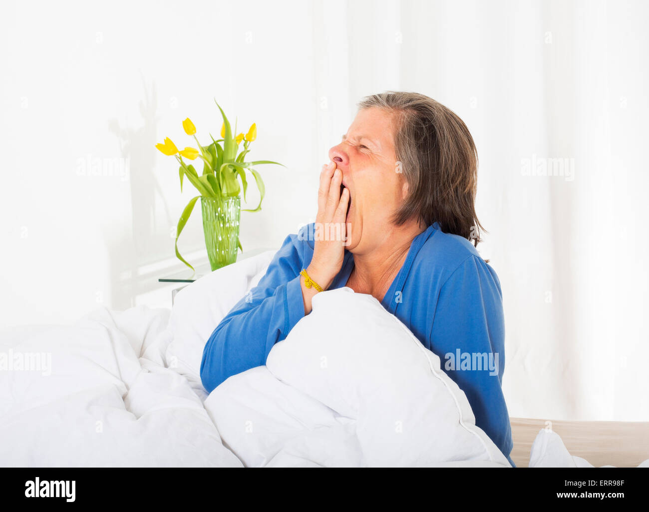 Frau in den Fünfzigern in ihrem Bett sitzen und aufstehen Stockfoto