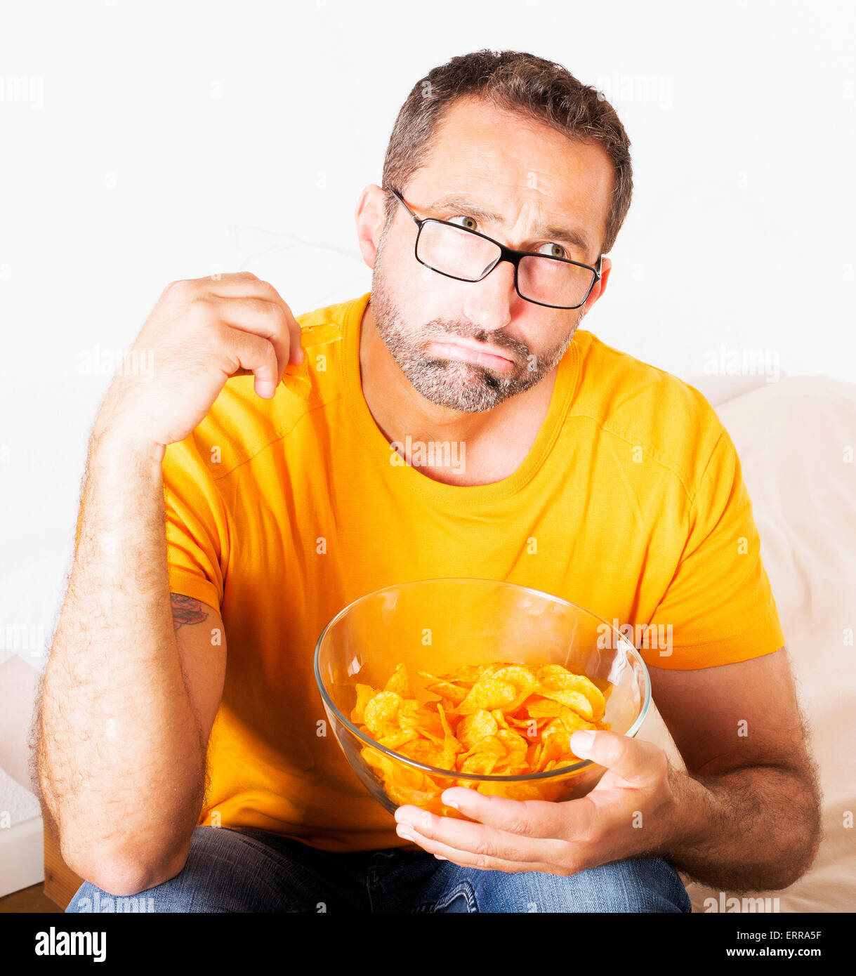 Mann mit Brille hält eine Schale mit Kartoffelchips und Essen Sie Stockfoto