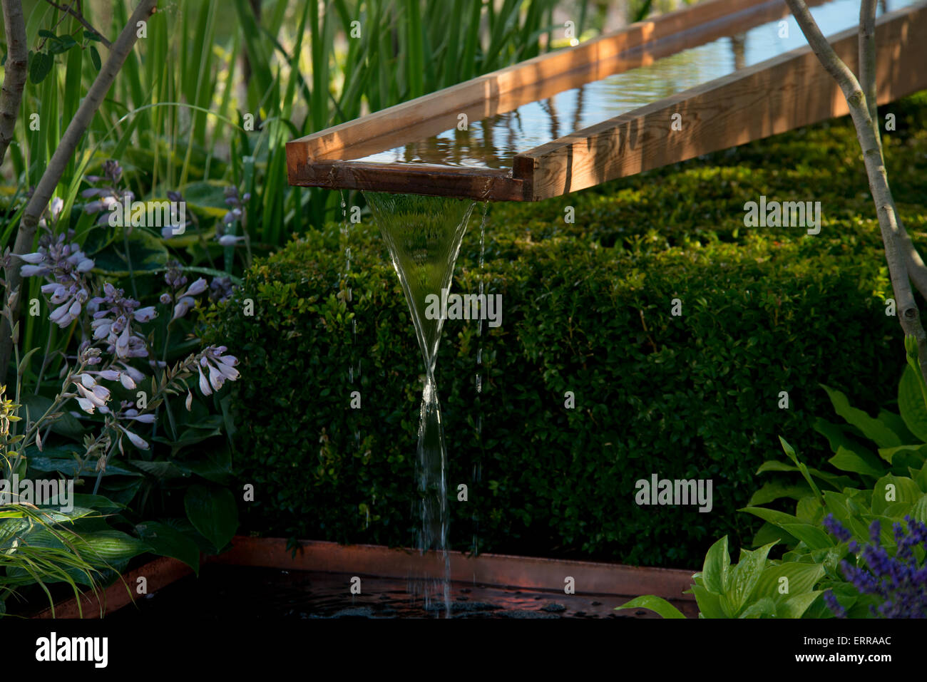 Wasser fließt über eine hölzerne Rill in einen Teich in der Vestra Reichtum Garten von The Hampton Court Flower Show, 2014 Stockfoto