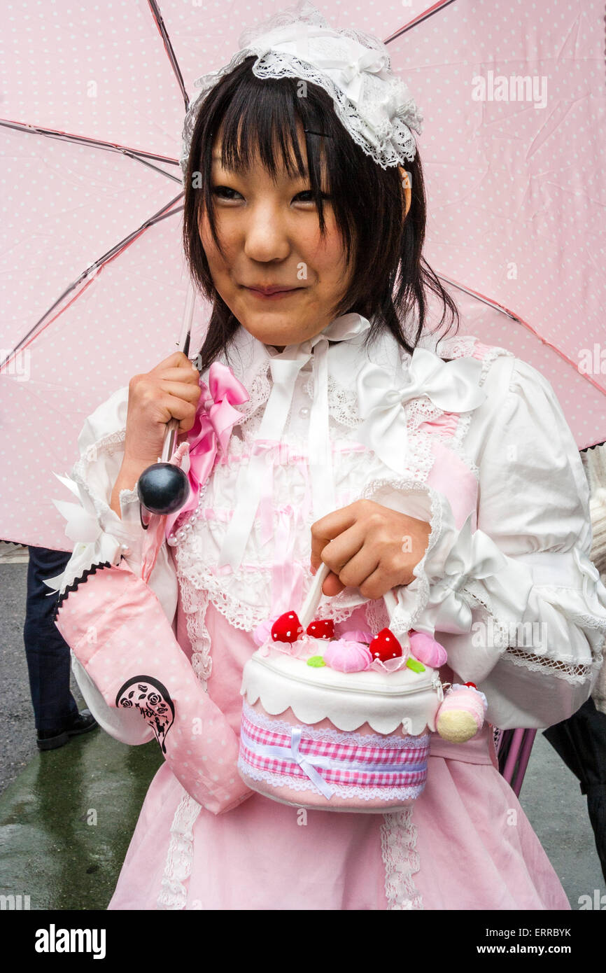 Japanische junge Frau im Stil von "Sweet Lolita" in Harajuku, Tokio. Tragen Sie rosafarbene und weiße Kleidung und halten Sie den rosafarbenen Regenschirm und die Kuchenhandtasche. Stockfoto