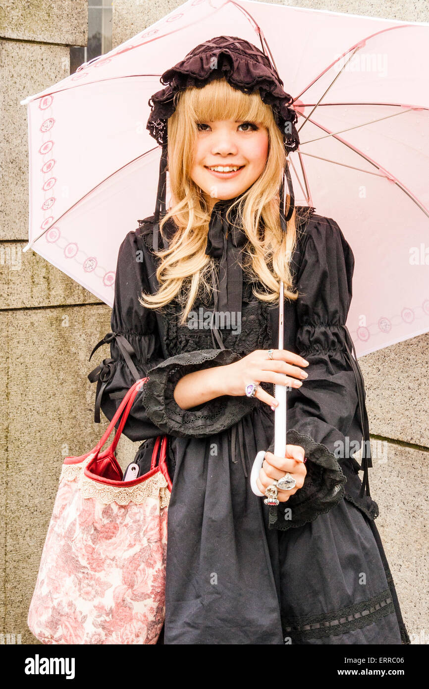 Harajuku, Tokio, eine junge japanische Frau, die sich in Lolita, rorita Fasshon, Modestil, stehend mit pinkfarbenem Regenschirm und lächelnd mit Augenkontakt bekleidet. Stockfoto