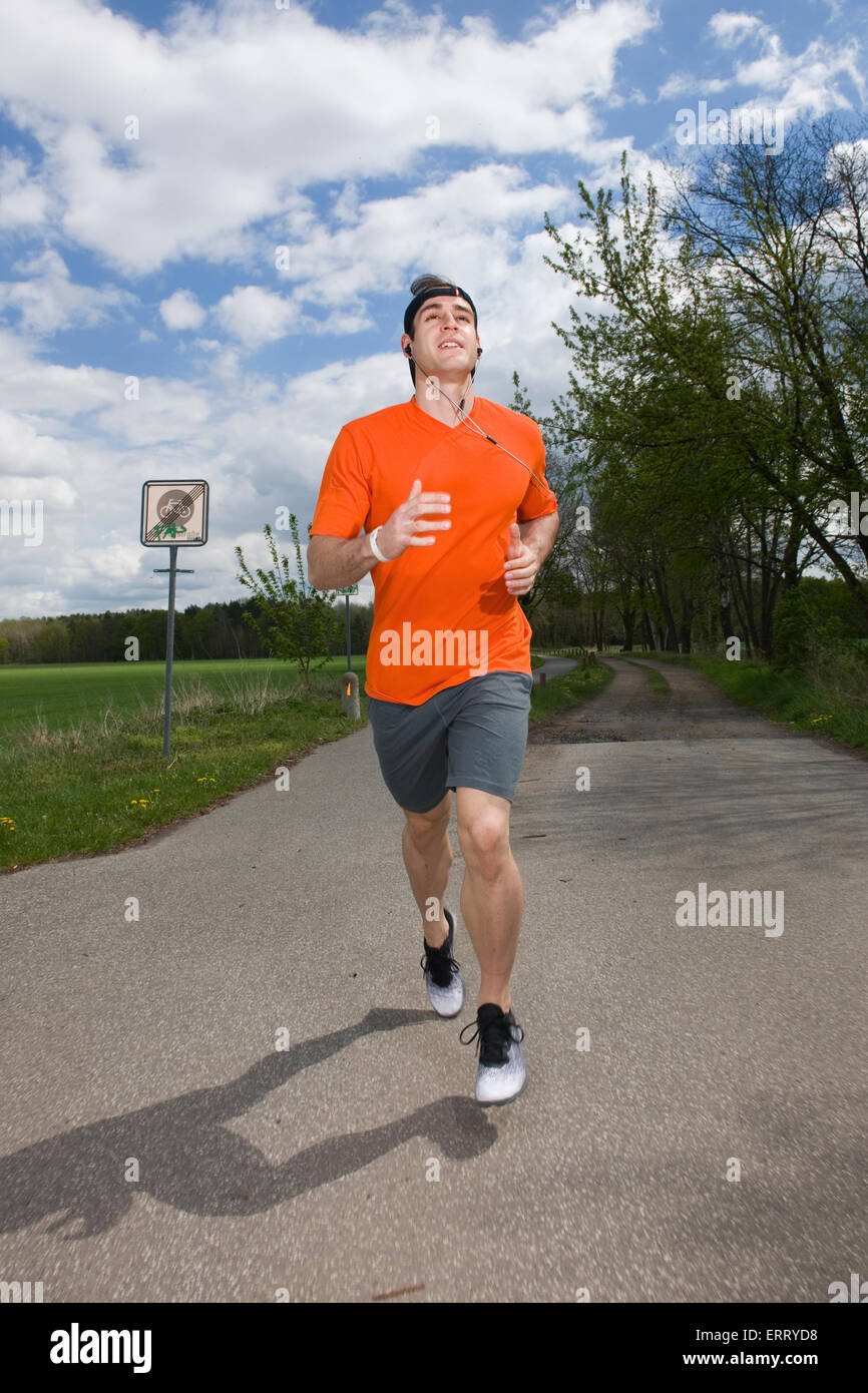 frontale Ganzkörper-Ansicht eines jungen Mannes in der orange Sport Kleid und Mütze auf ein gepflasterter Weg in Richtung der Kamera kontinuierlich Stockfoto