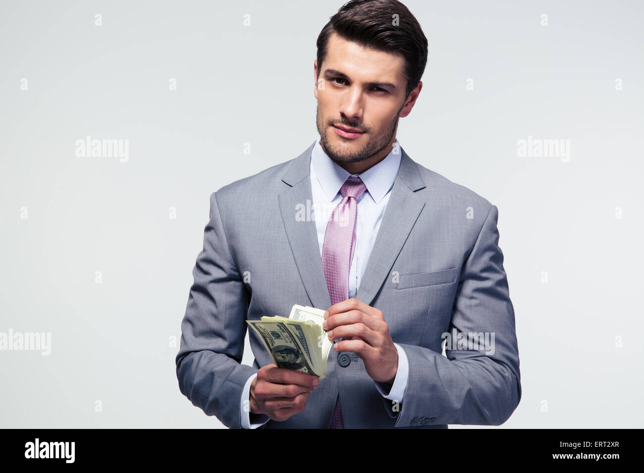 Gut aussehend Geschäftsmann zählen US-Dollar über grauen Hintergrund und Blick in die Kamera Stockfoto