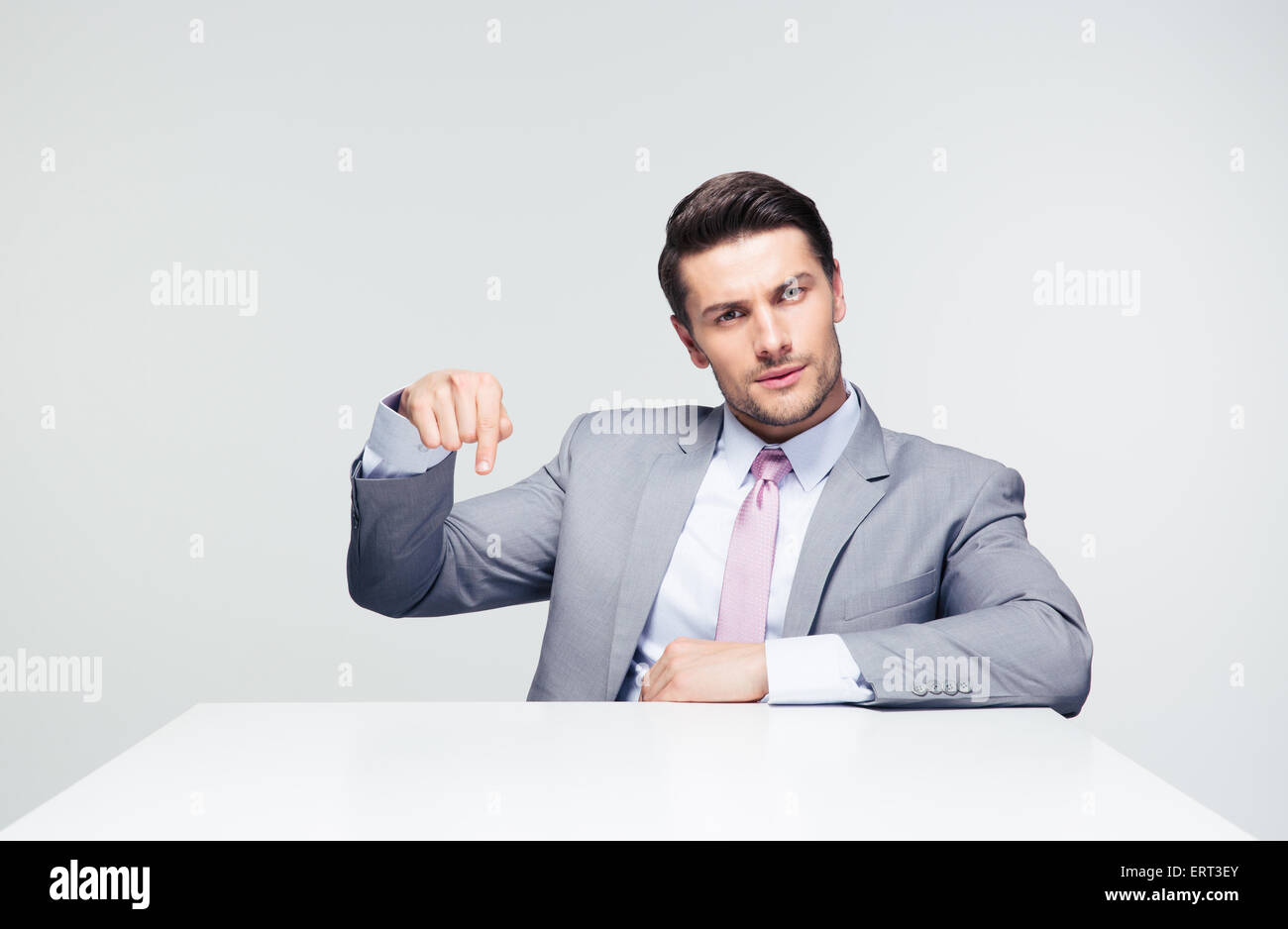 Zuversichtlich Geschäftsmann auf den Zeigefinger Tisch sitzen auf grauem Hintergrund. Loooking in die Kamera Stockfoto