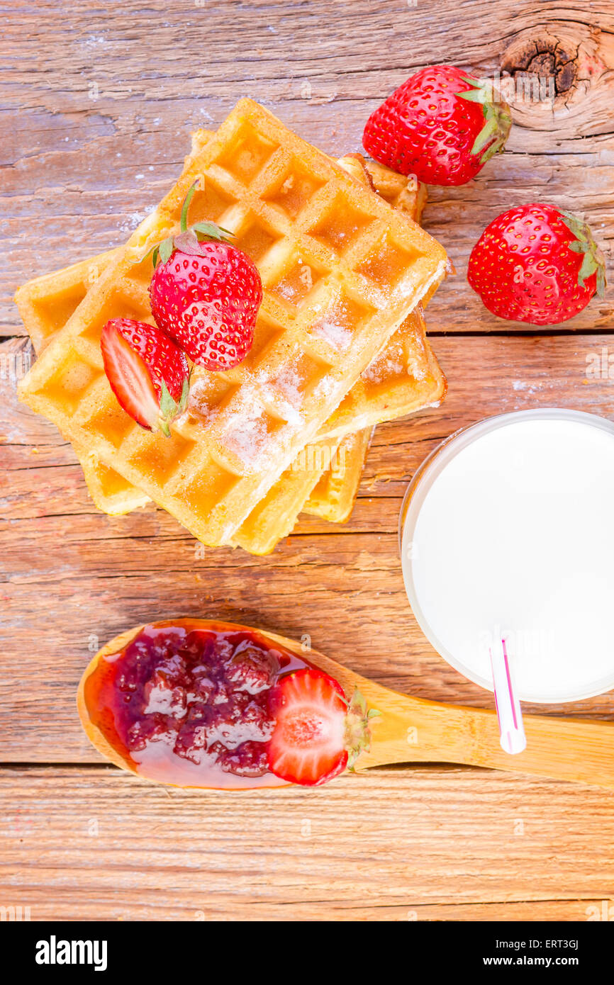 hausgemachte Waffeln mit Erdbeer-Marmelade und Glas mit Milch auf hölzernen Hintergrund Stockfoto