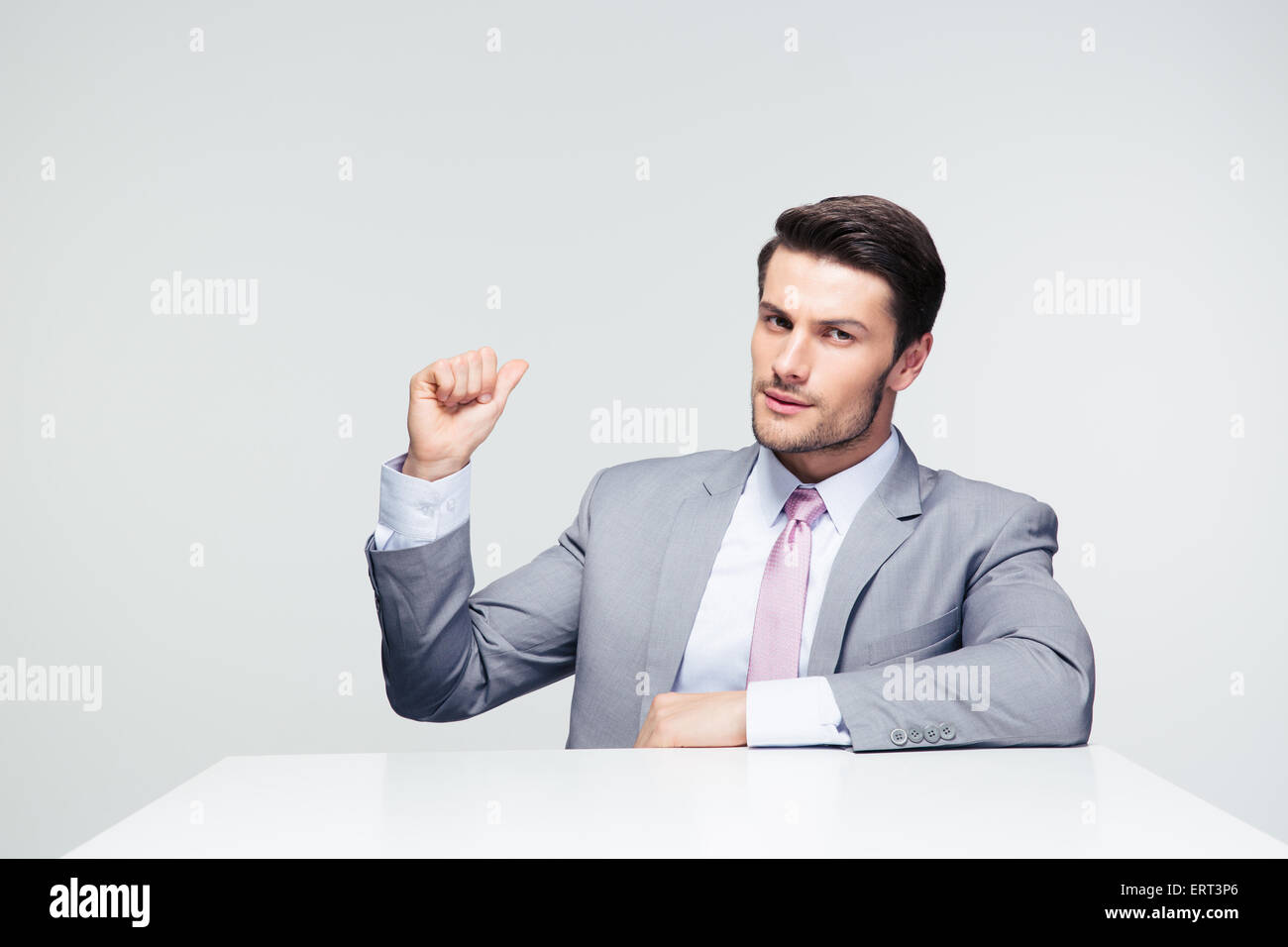 Zuversichtlich, Geschäftsmann, sitzen auf den Tisch Zeigefinger wieder über grauen Hintergrund Stockfoto