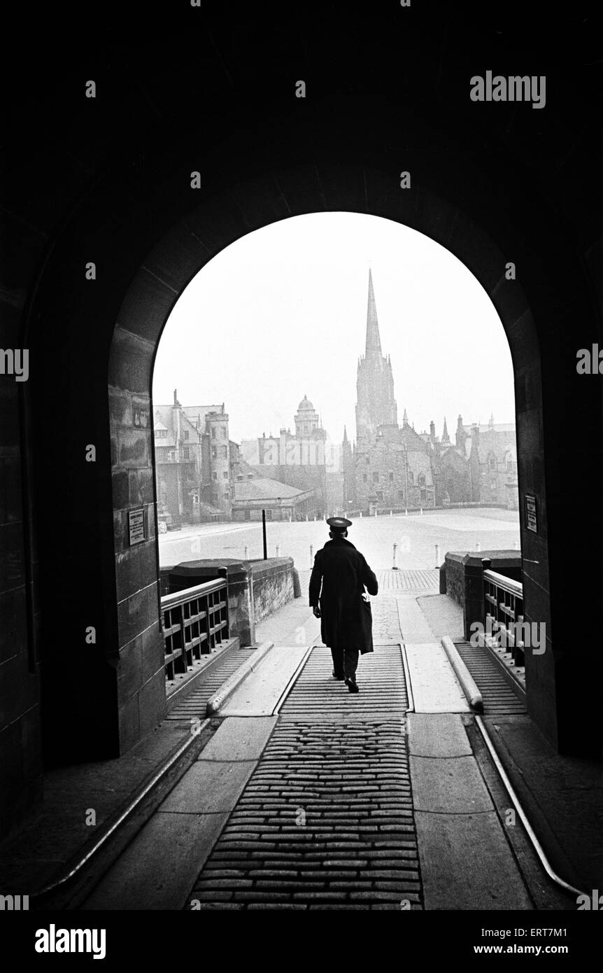 Ein Mann, der hilft die Zeit Waffe zu Fuß durch den Eingang Torbogen zum Edinburgh Castle, betreiben Blick auf die Altstadt Stadt gesehen durch den Torbogen, ca. 1945. Stockfoto