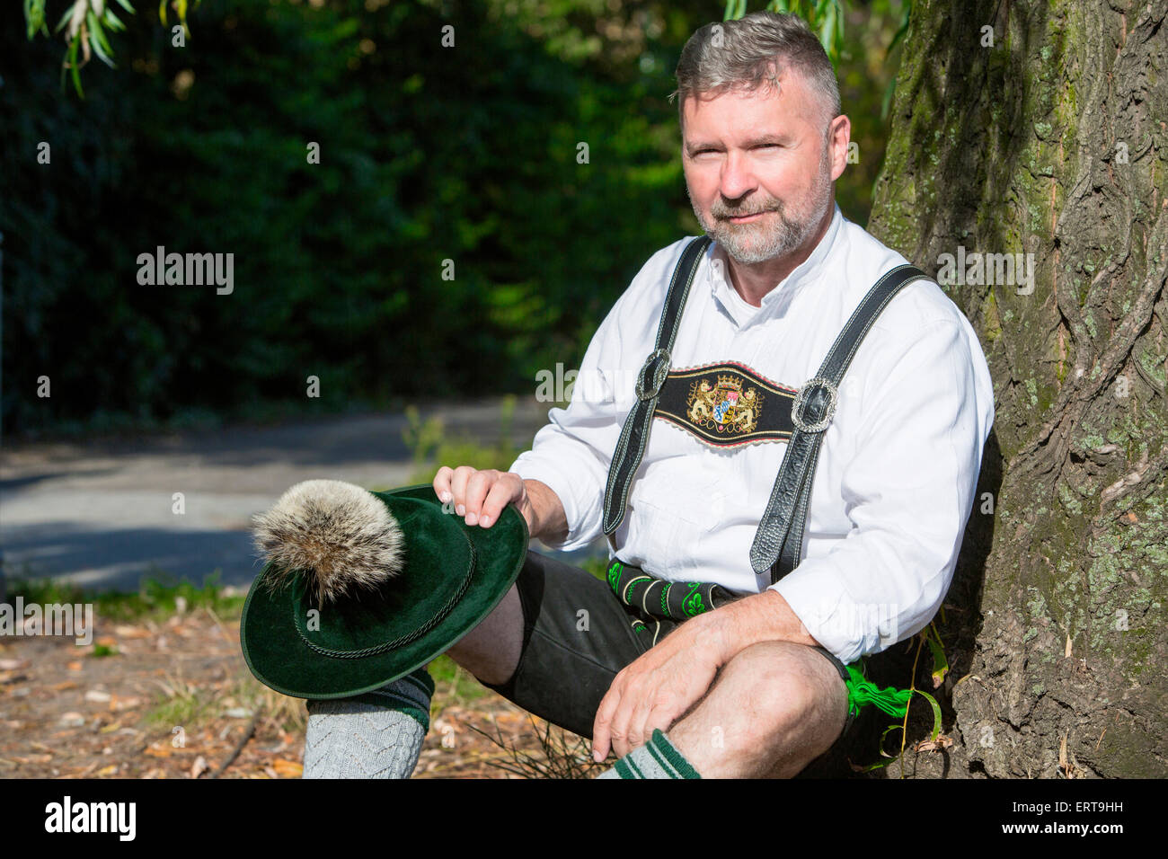 Mann in bayerischer Tracht, die von einem Baum zu sitzen Stockfoto