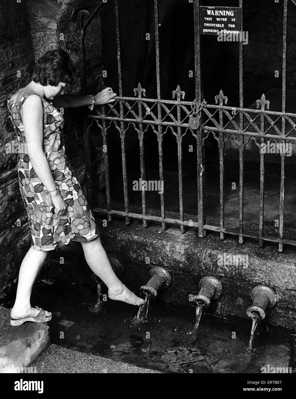 Heather Doney benetzt ihren Fuß auf das Rohr im Brunnen Lane an Liskeard, Cornwall.  Heather war im Anschluss an eine uralte Brauch in denen Wasser von jedem der vier Rohre die geheimnisvolle Eigenschaft, dafür zu sorgen haben soll eine Mädchen werden früh heiraten. 29. September 1966. Stockfoto