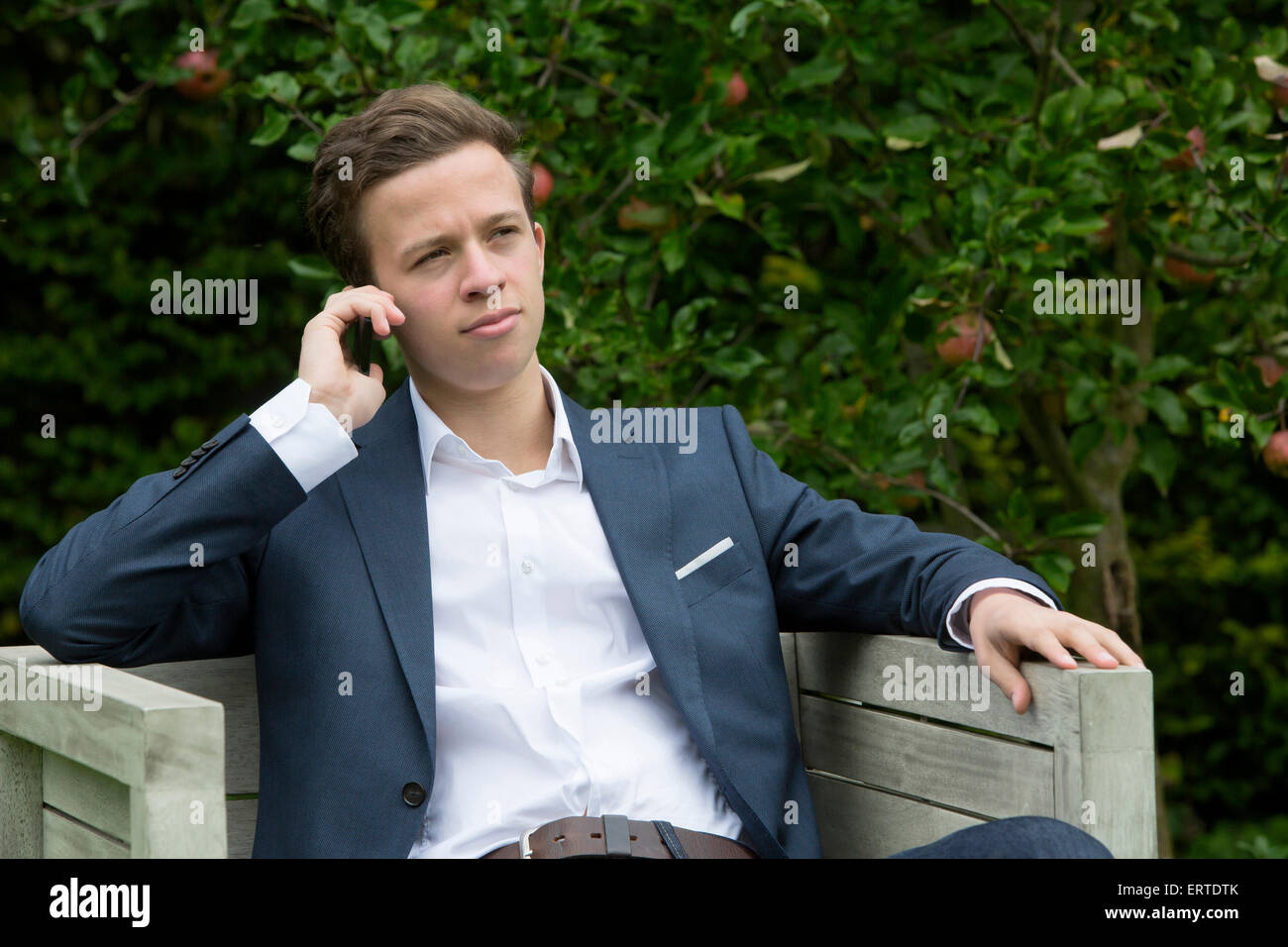 junger Mann in einem Anzug sitzen draußen am Telefon sprechen Stockfoto