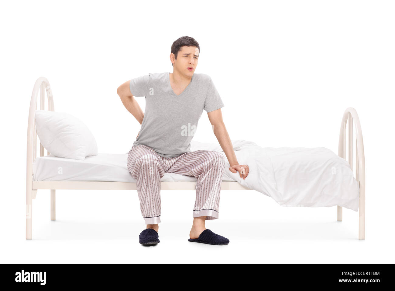 Junger Mann mit einer rückseitigen Schmerz sitzt auf einem Bett in seinem Pyjama isoliert auf weißem Hintergrund Stockfoto
