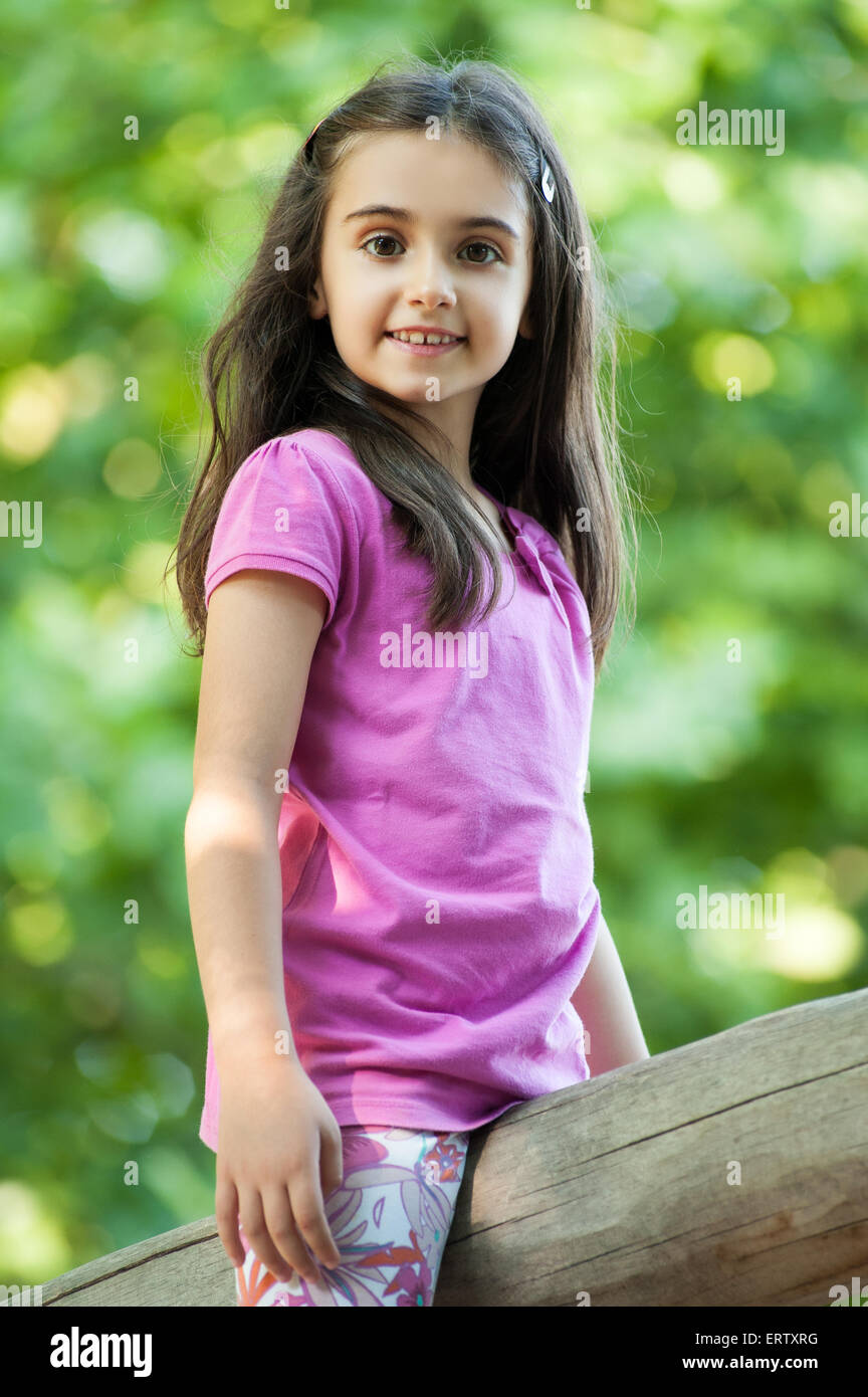 Niedliche kleine Mädchen sitzen im freien gegen grüne Blätter beiderseits eine Holzstange Stockfoto