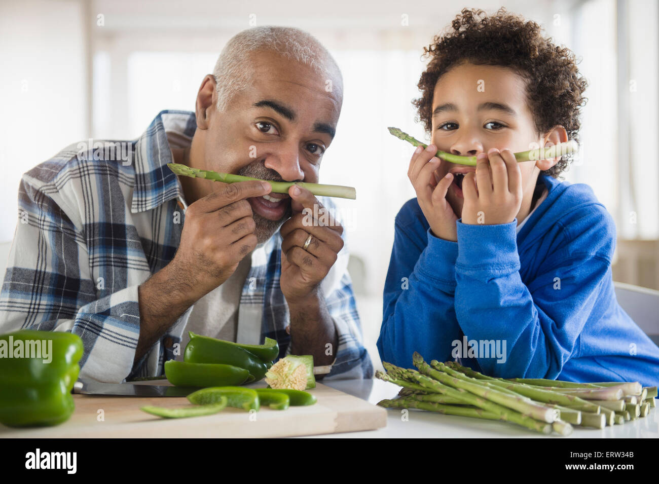 Gemischte Rassen Großvater und Enkel machen Schnurrbärte mit Spargel Stockfoto