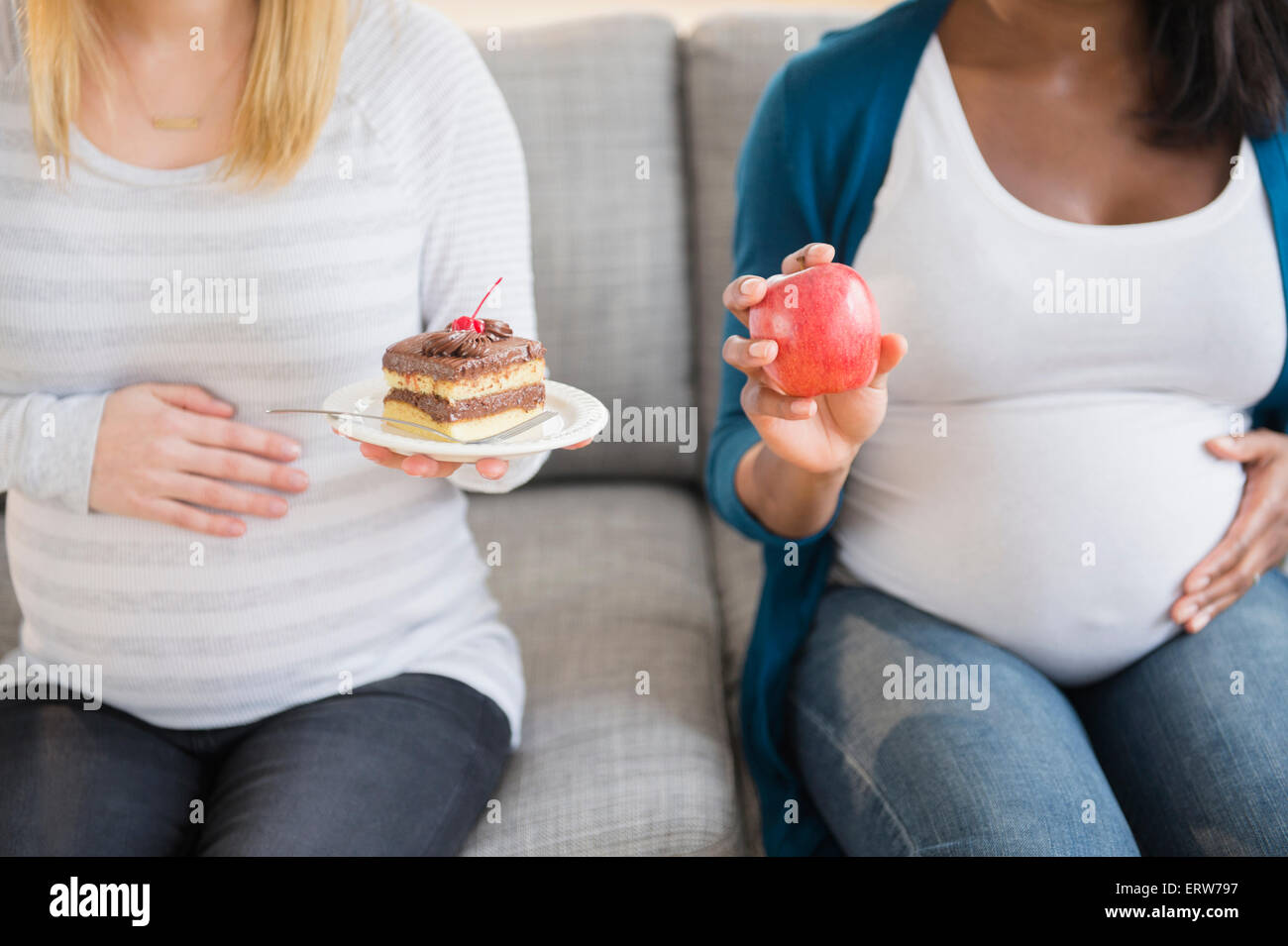 Schwangere Frauen vergleichen, Apfel und Kuchen auf sofa Stockfoto