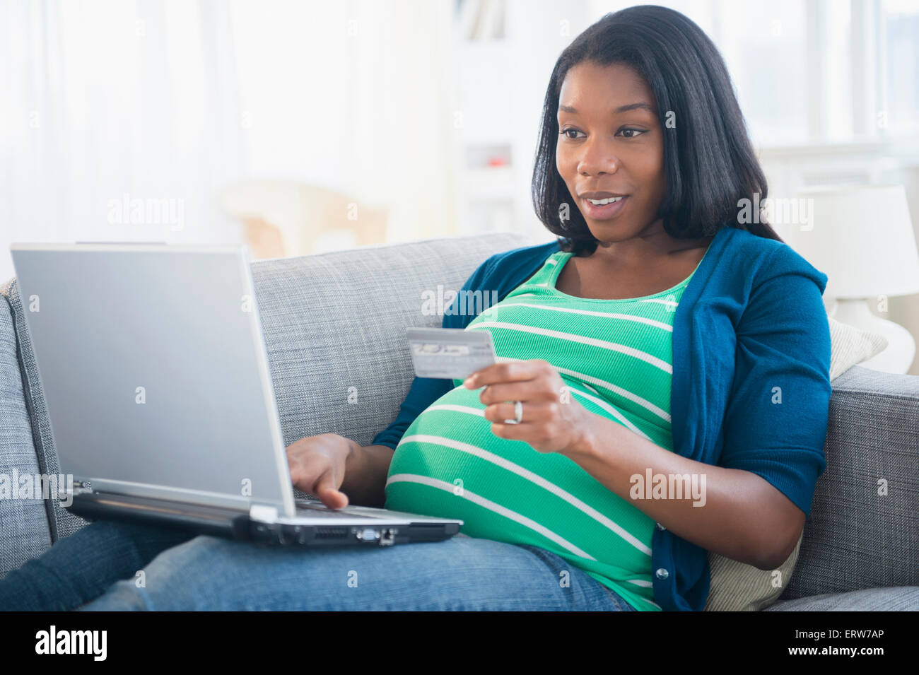 Schwarze schwangere Frau online-shopping auf sofa Stockfoto