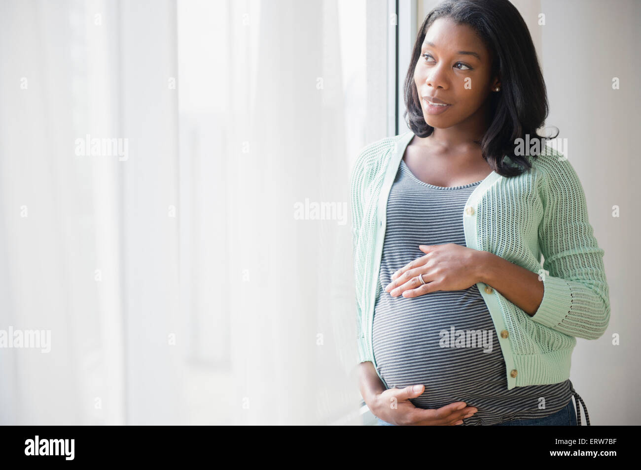 Schwarze schwangere Frau hält ihren Bauch am Fenster Stockfoto