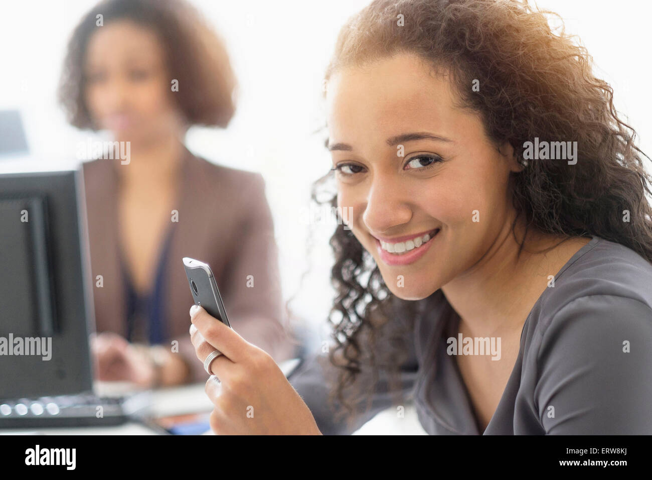 Geschäftsfrau, die lächelnd mit Handy im Büro Stockfoto