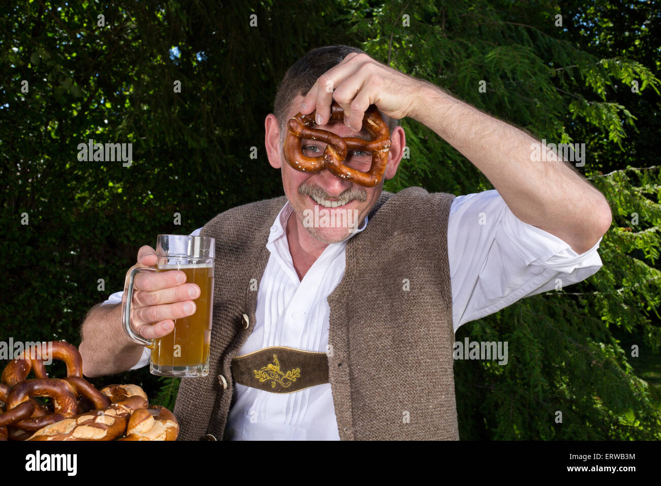 bayerischen Mann sitzt auf der Bank mit einem Bierkrug und Brezel Stockfoto