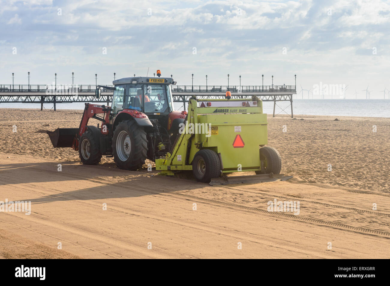 Ein Traktor zieht sich entlang einer "Barbier" "Surf Rake" Maschine zu reinigen den Strand und Sand Rechen. In Skegness, Lincolnshire, England Stockfoto