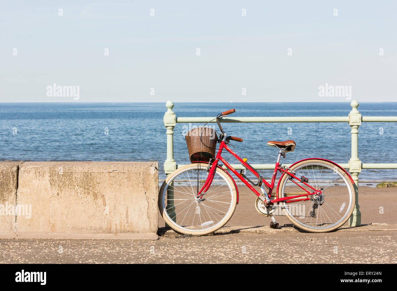 Ein rotes Fahrrad mit einem Korb auf der Vorderseite auf dem Deich von einem Strand in Schottland an einem Sommertag Stockfoto