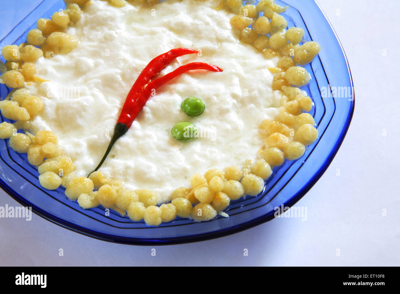 Garnieren Sie Gemüsesalat Boondi raita mit grünen Erbsen und roten Chili in einer blauen runden Glasschale auf weißem Hintergrund Stockfoto