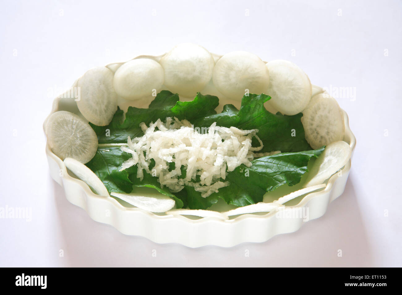 Grünes Gemüse; Runde Scheiben von Muli Rettich Raphanus Sativa mit grünen Blättern auf weißem Hintergrund Stockfoto