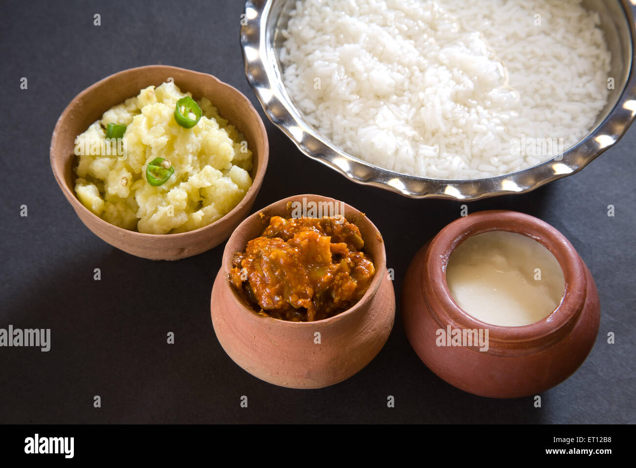Indische Mittagessen Pakhala Reis in Schale und Gurke Maische Kartoffel mit Chili-Joghurt in irdenen Topf schwarzen Hintergrund Stockfoto