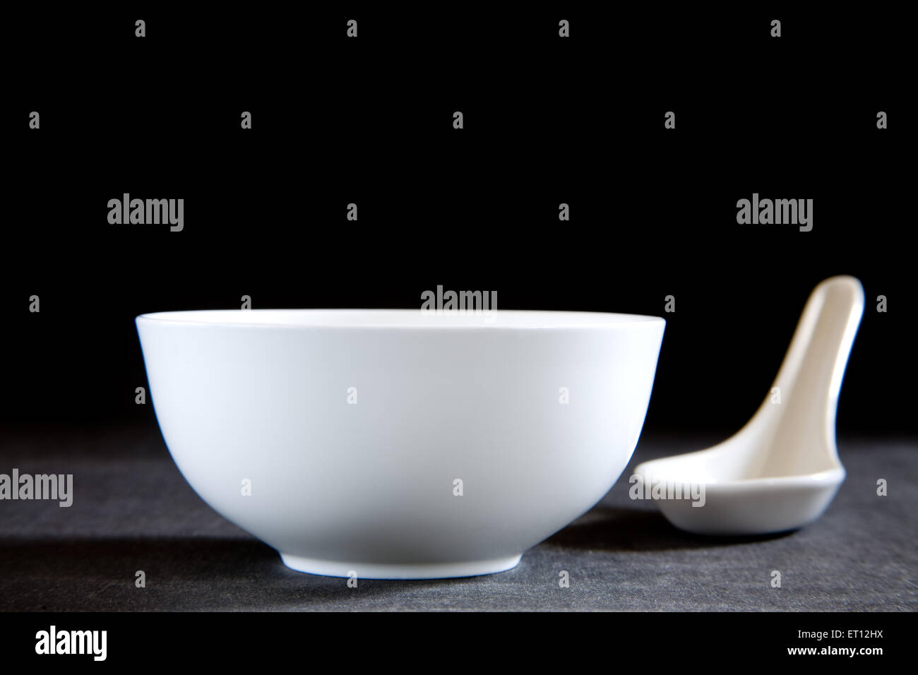 Runde Keramikschüssel, weißer Löffel, schwarzer Hintergrund Stockfoto