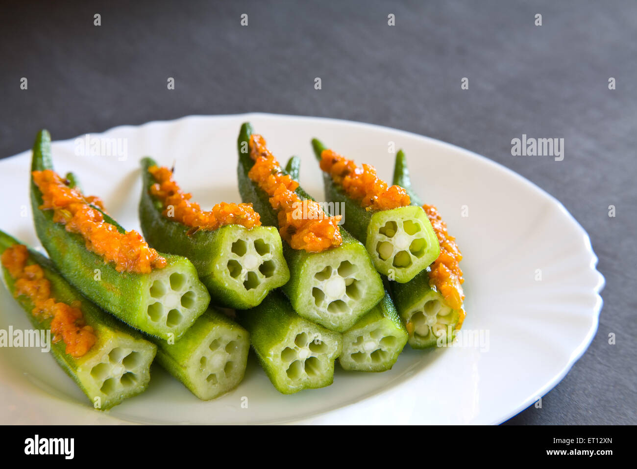 Mit Fingern gefülltes Okra-Gemüse in weißer Keramikplatte auf schwarzem Hintergrund Stockfoto