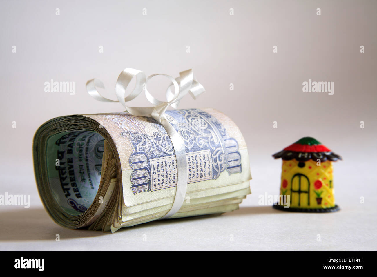 Home-Modell aus Kunststoff und Bündel von hundert Rupien Noten auf weißem Hintergrund Stockfoto