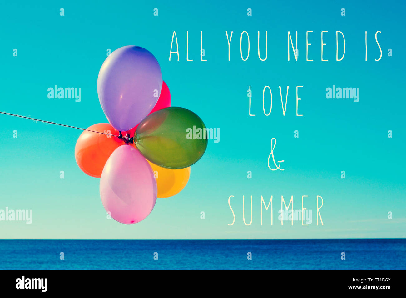 einem Haufen Luftballons in verschiedenen Farben gegen den blauen Himmel mit dem Meer im Hintergrund und der Text alle Sie brauchen ist Liebe ein Stockfoto