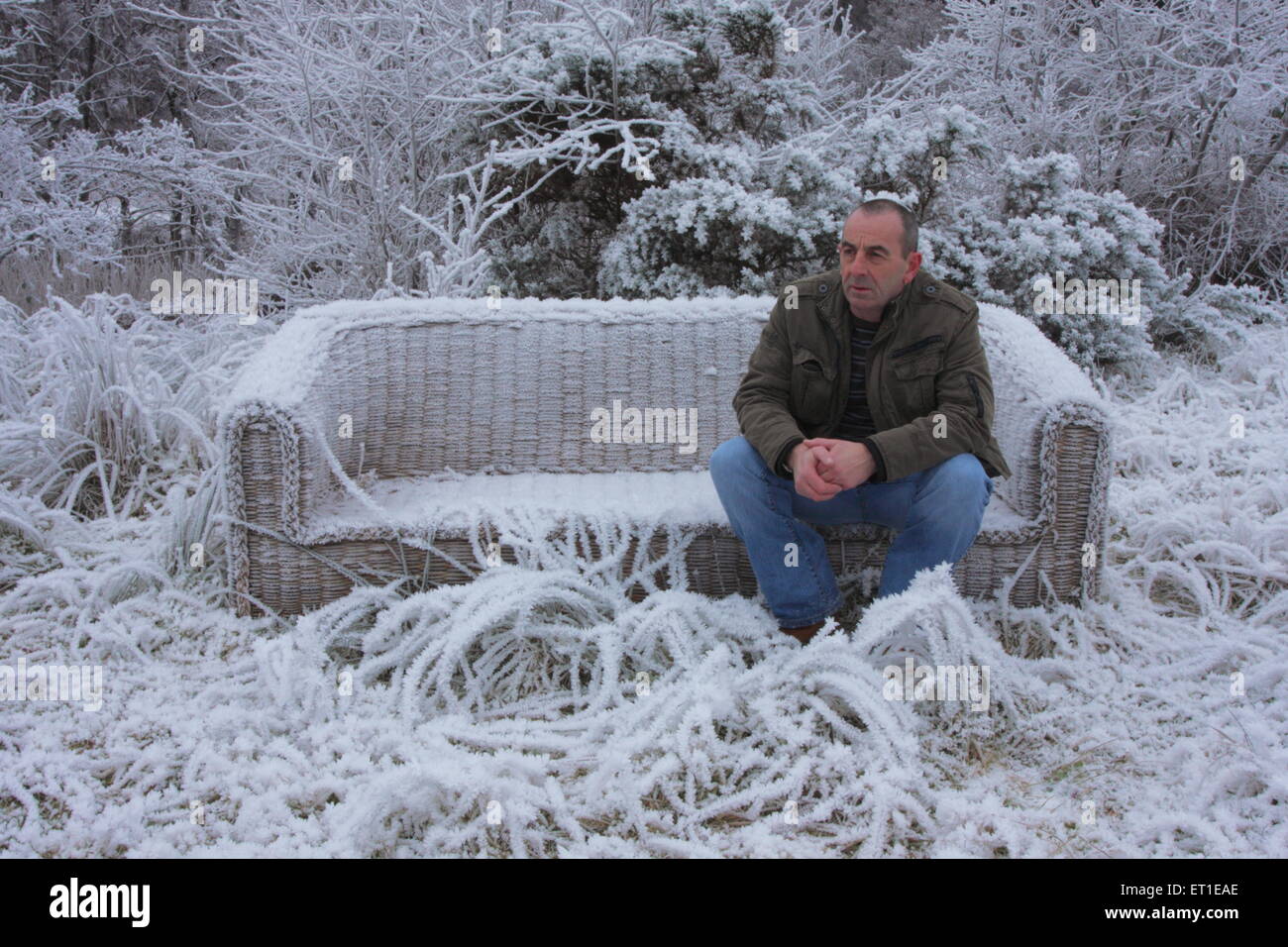 Mann sitzt auf aufgegeben, gedumpten Frost bedeckt Sofa im Winter. Stockfoto