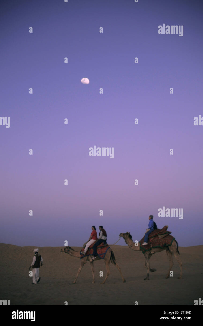 Touristen sitzen auf Kamelen fallen Nacht mit Mond am Sam Sanddünen; Jaisalmer; Rajasthan; Indien Stockfoto