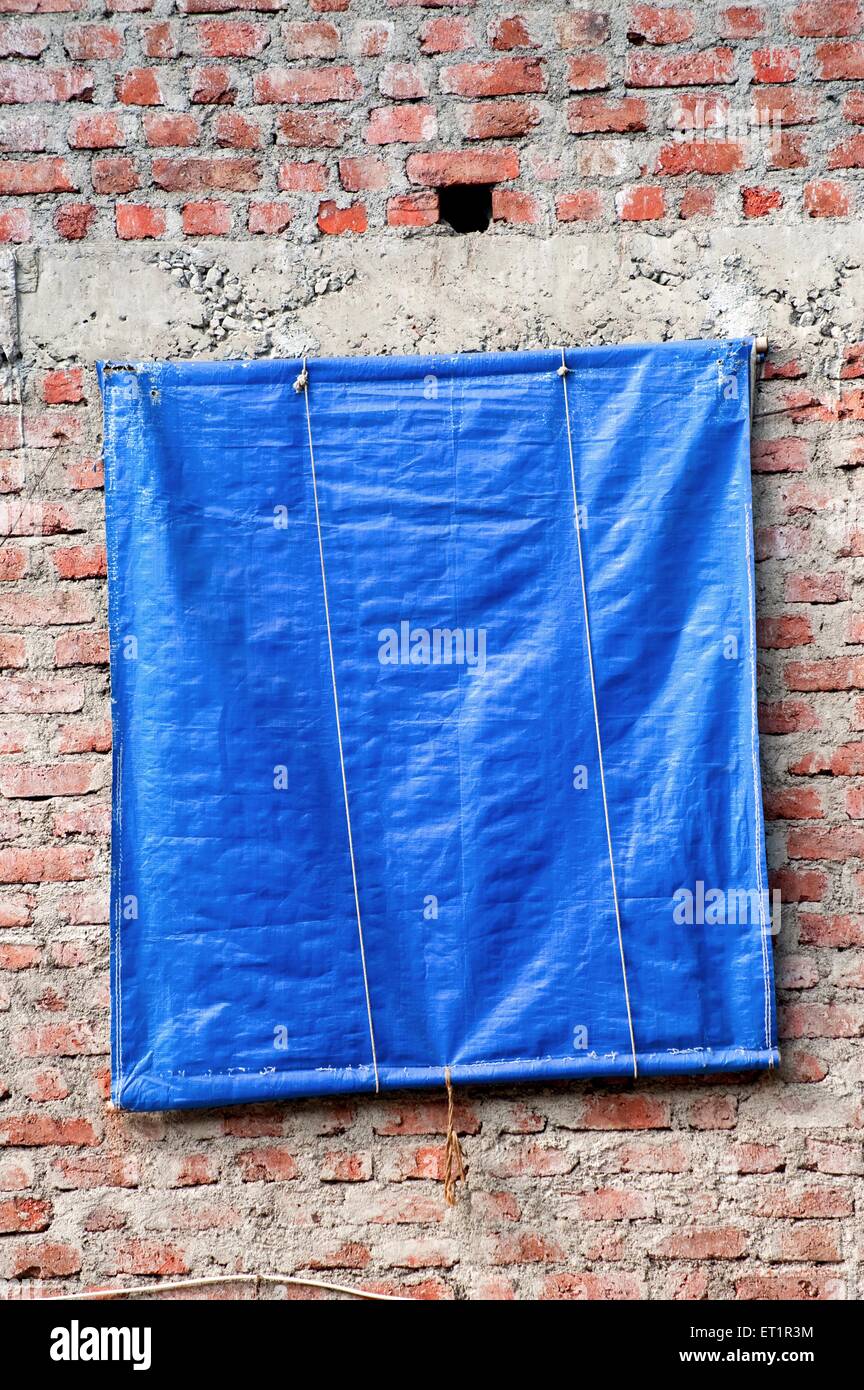 Blaue Kunststoff-Plane Fenstervorhang Abdeckung auf Ziegelwand in Indien Stockfoto