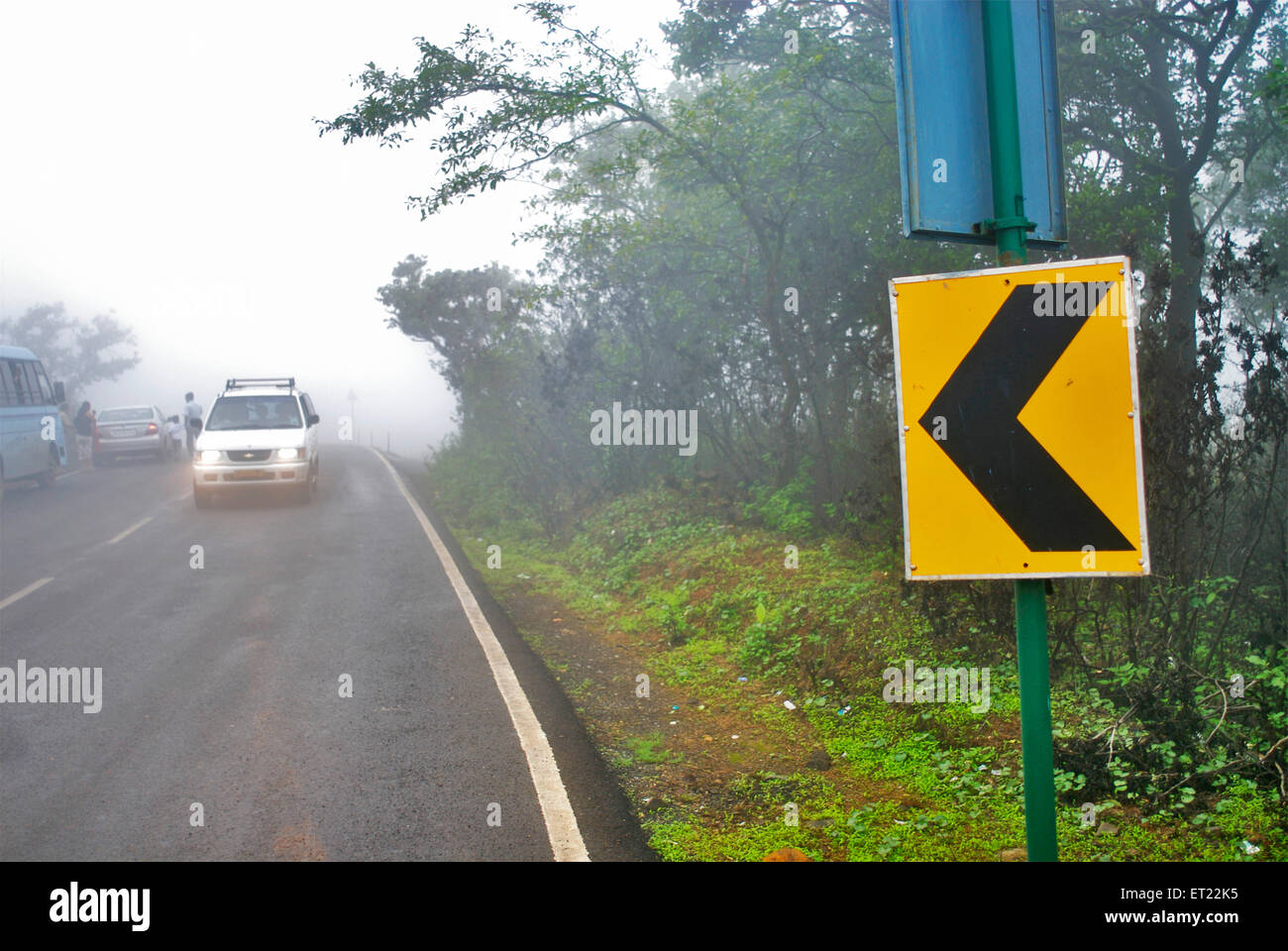 Ein weißes Auto auf ein Schild Richtung an einem nebligen Tag im Tiger Hills zukommen; Lonavala; Maharashtra; Indien Stockfoto