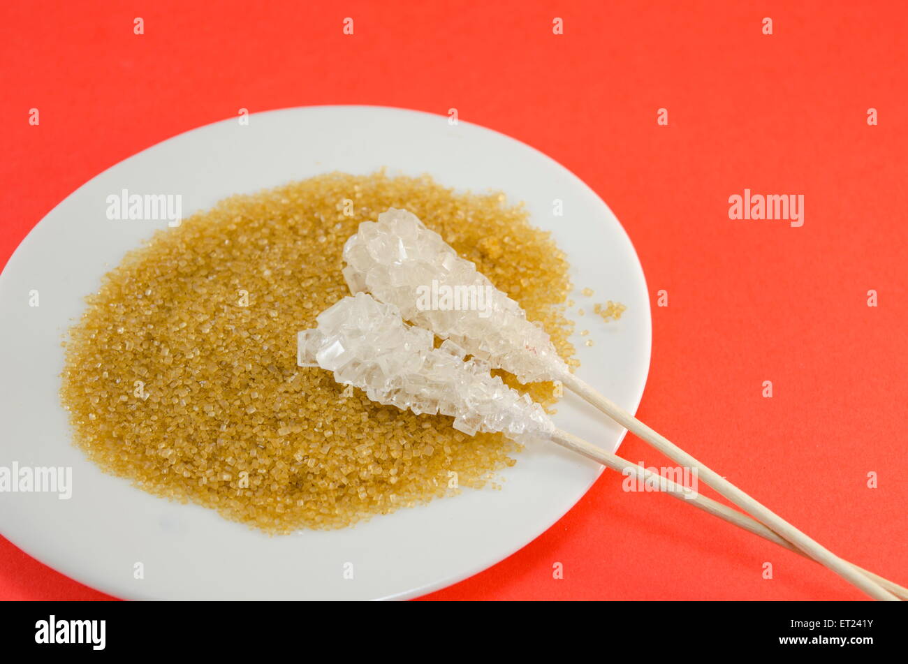 Zwei Zuckersticks mit weißen und braunen Zucker in einem schwarzen Teller vor einem roten Hintergrund Stockfoto