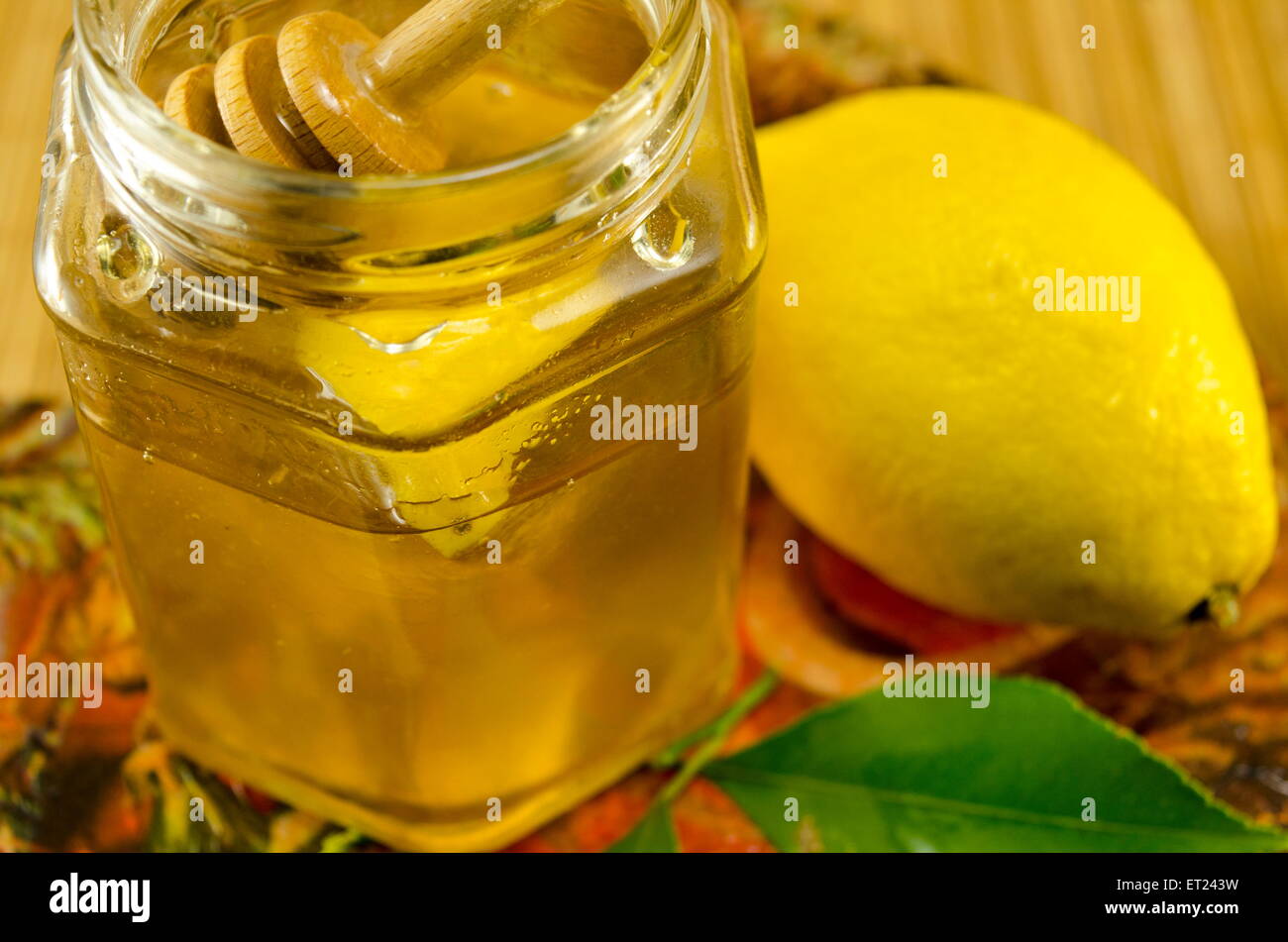 Glas mit einem hölzernen Löffel Honig und Zitrone auf einem Tisch Stockfoto