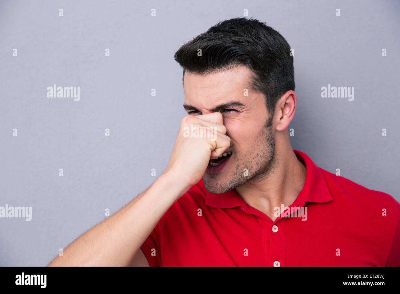 Legerer Mann für seine Nase mit der Hand über grauen Hintergrund Stockfoto