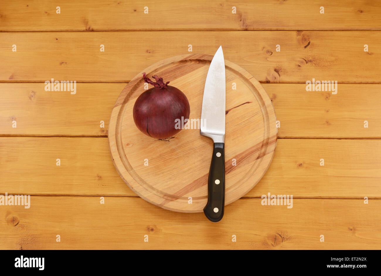 Ganze rohe rote Zwiebel mit einem scharfen Küchenmesser auf ein Schneidbrett aus Holz Stockfoto