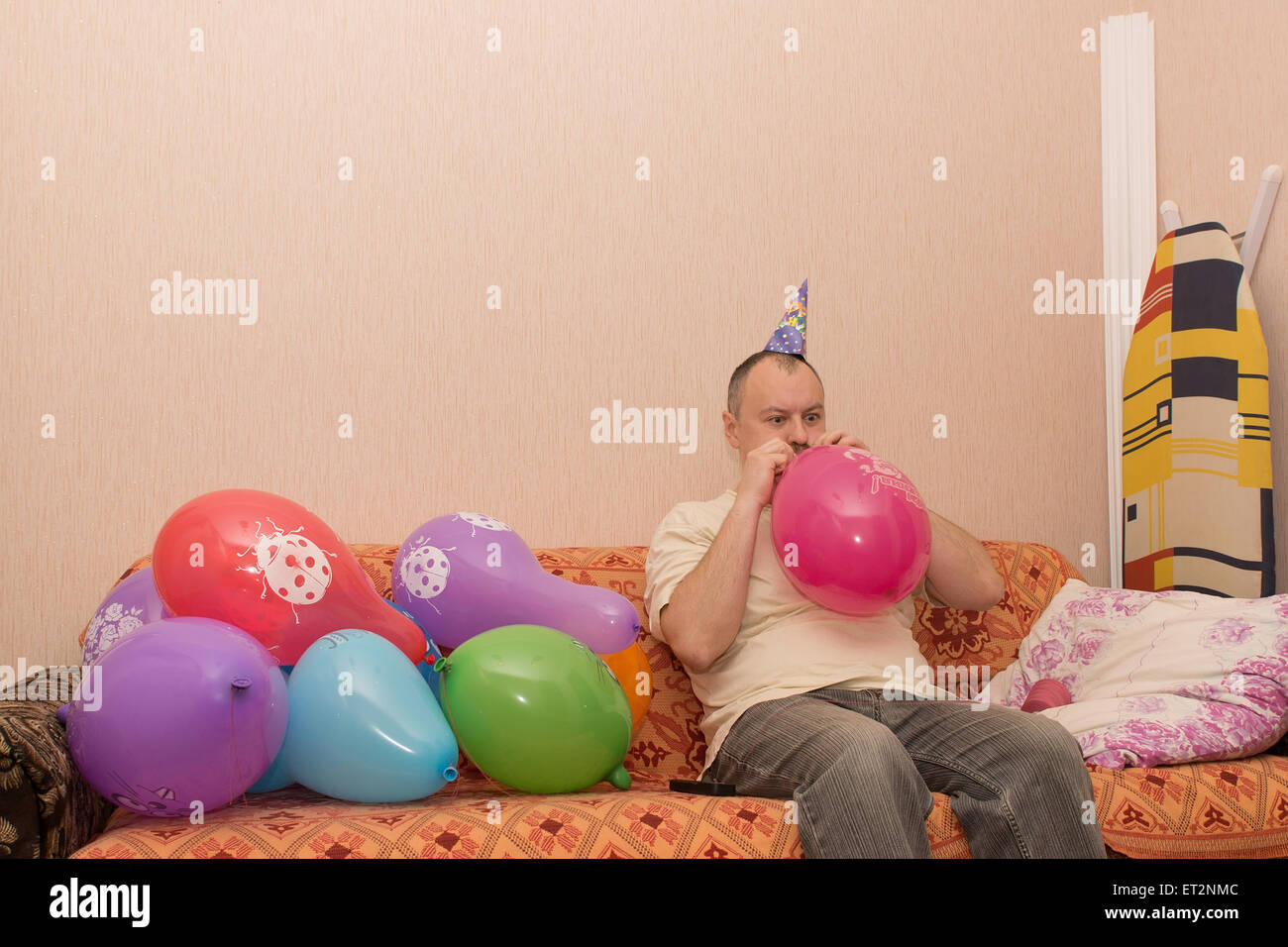 Mann mit dem Hut auf der Couch sitzen und bläst den Ball Stockfoto